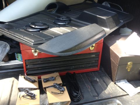 1979 Ford Bronco - The cargo area of a vehicle holds black floor mats, speakers, a red toolbox, and various wiring components.