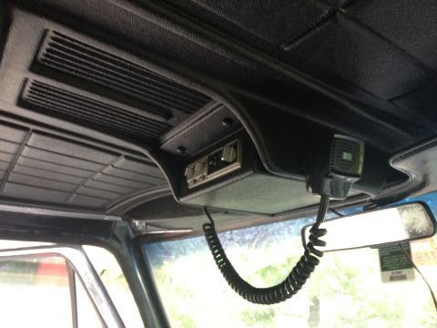 1979 Ford Bronco - The interior of a vehicle shows a CB radio mounted to the headliner, complete with a coiled cord and microphone.