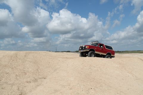 1990 Ford Bronco - This red 1990 Ford Bronco is equipped with off-road lights and is navigating a sandy terrain.