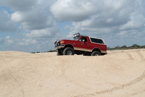 1990 Ford Bronco - This lifted Ford Bronco is navigating a sandy terrain with a cloudy sky overhead.