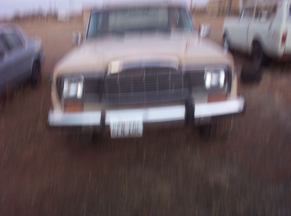 Motion-blurred front view of a tan full-size Jeep wagon parked in a dead grass field