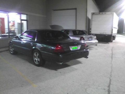 2003 Ford Crown Victoria - A dark sedan is parked in a lot at night, with other vehicles visible in the background.