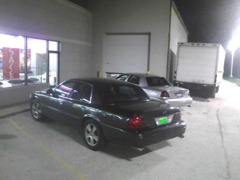 2003 Ford Crown Victoria - Two sedans and a box truck are parked outside a building at night.