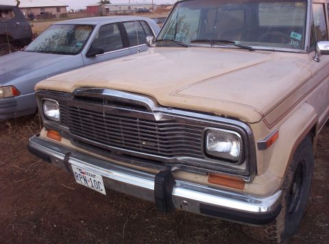 1988 Ford Bronco - Front view of a 1984 Jeep Grand Wagoneer, parked next to a silver sedan.