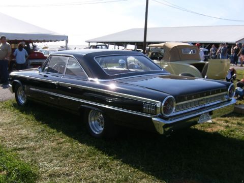 1963 Ford Galaxie - A black 1963 Ford Galaxie coupe is displayed outdoors with other vehicles and tents in the background.