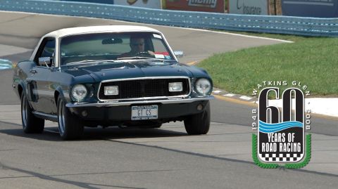 1968 Ford Mustang - A dark green 1968 Ford Mustang coupe with a white roof drives on a race track, with a "60 Years of Road Racing" logo visible.