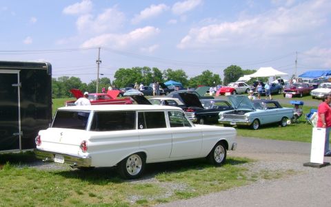 1965 Ford Falcon - A white station wagon is parked at an outdoor car show with several other vehicles visible in the background.