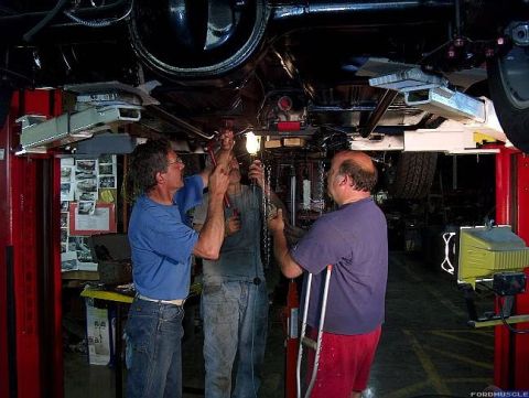 1968 Shelby GT350 - Mechanics inspect the undercarriage of a car on a lift, with tools and equipment visible.