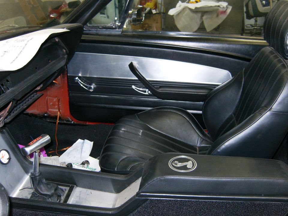 Black interior of a convertible mid-restoration with bucket seat, console and exposed door frame