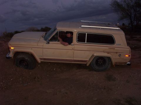 1988 Ford Bronco - A tan Jeep Cherokee Chief is driven off-road under a cloudy sky.