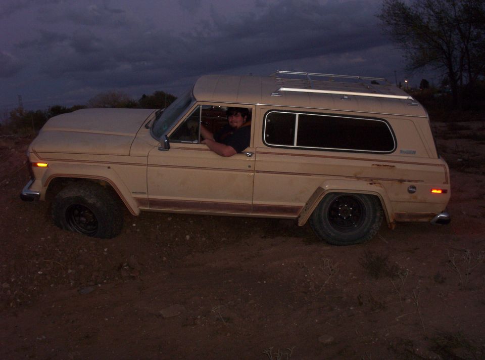 Tan two-door Jeep Cherokee Chief on black steel wheels parked on dirt at dusk