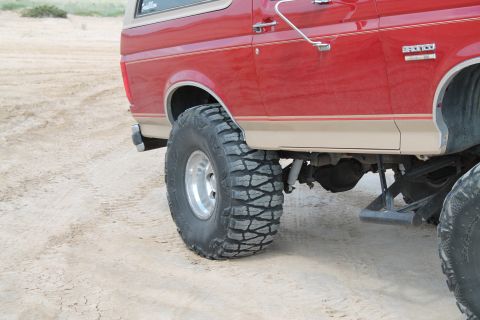 1990 Ford Bronco - Side view of a red 1990 Ford Bronco modified with large off-road tires and suspension.