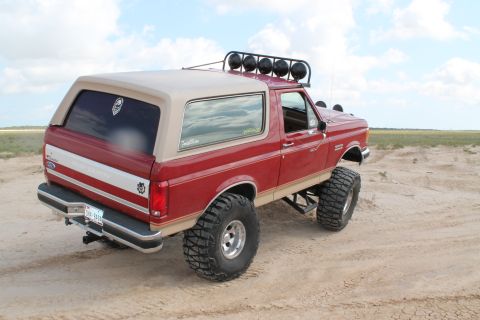 1990 Ford Bronco - This lifted Ford Bronco is ready for adventure on a sandy landscape under a cloudy sky.