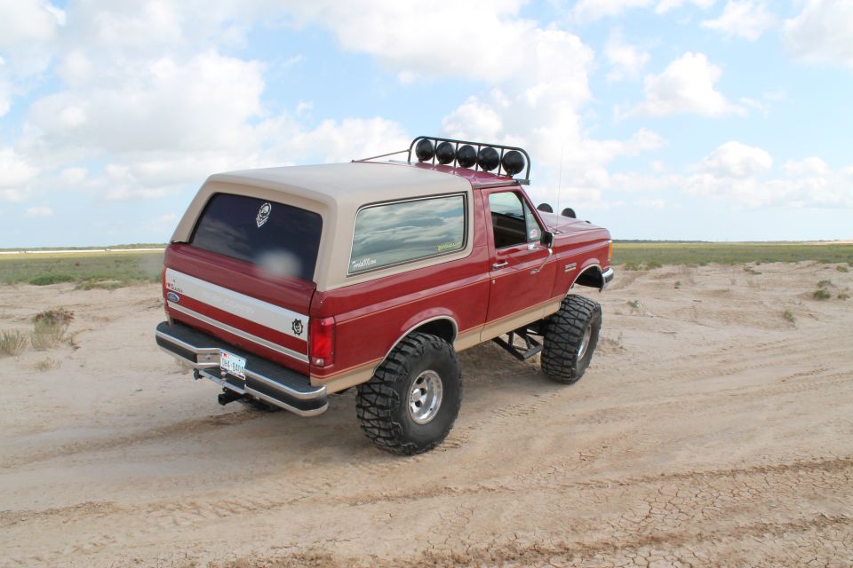 Red 1990 Ford Bronco with tan top, lifted suspension, and off-road tires on sandy terrain