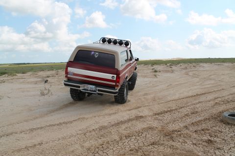1990 Ford Bronco - This 1990 Ford Bronco is captured from the rear, equipped with off-road tires and a light bar, navigating a dry, cracked terrain under a cl…