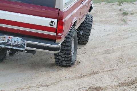 1990 Ford Bronco - Rear view of a red 1990 Ford Bronco modified with large off-road tires and a "Rough Country" decal.