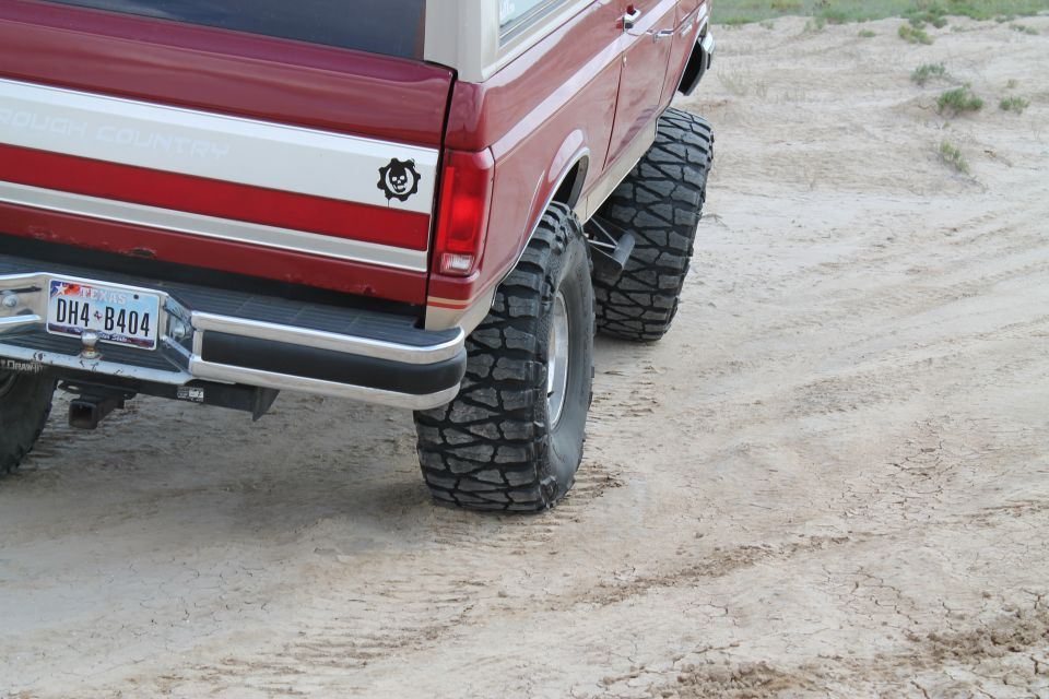 Red 1990 Ford Bronco with "Rough Country" decal and large off-road tires, rear view