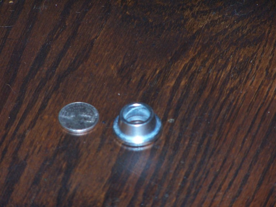 Metal grommet next to a penny on a wooden surface