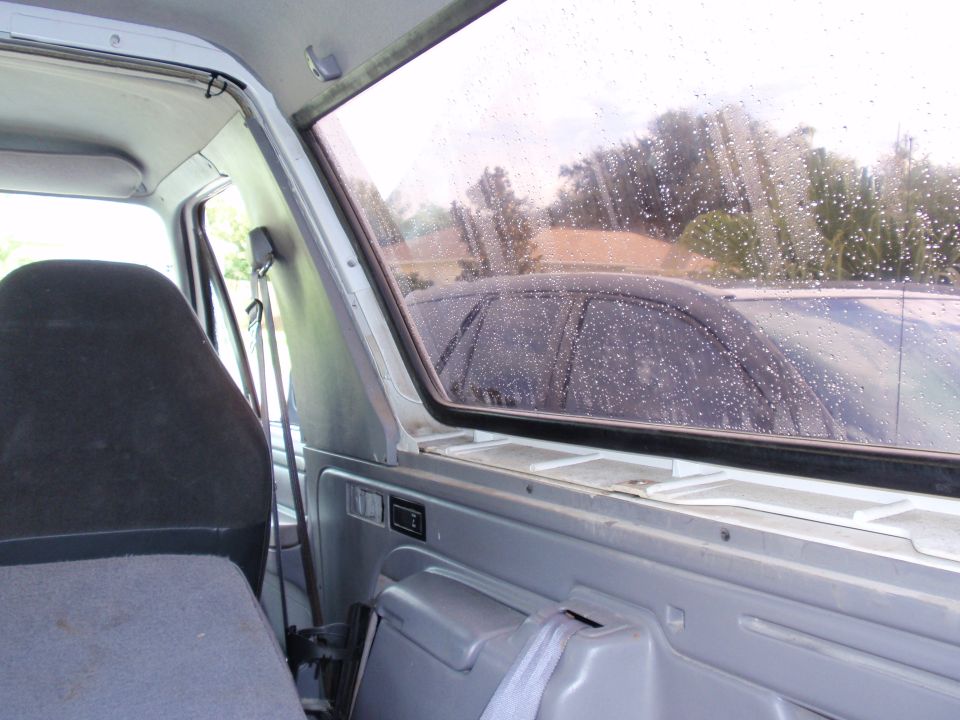 Interior of a truck cab looking out rear sliding window on a rainy day