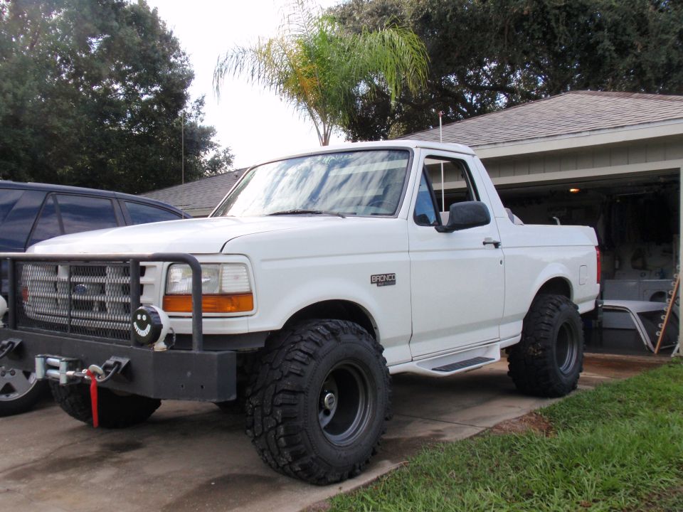 White Ford Bronco with a brush guard, winch, and large tires parked in a driveway