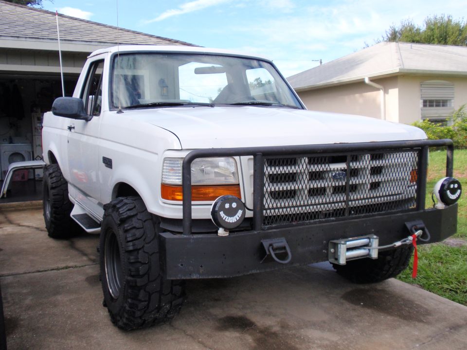 White Ford Bronco with bull bar, winch, and large tires parked in driveway