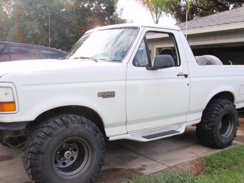 1995 Ford Bronco - A white Ford Bronco is parked in a driveway, showing its side profile and large off-road tires.