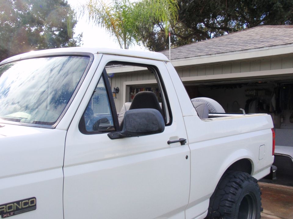 White Ford Bronco XLT side view, showing the driver's side door, window, side mirror, and rear cargo area with a spare tire cover