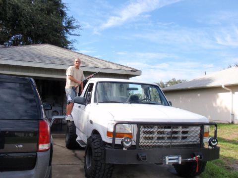 1995 Ford Bronco - A man stands on the door of a white pickup truck, which is parked next to a dark SUV.