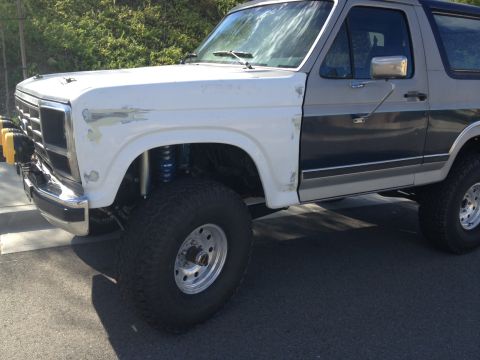 1986 Ford Bronco - This lifted Ford Bronco shows a two-tone paint scheme with a white front fender and gray side panel.