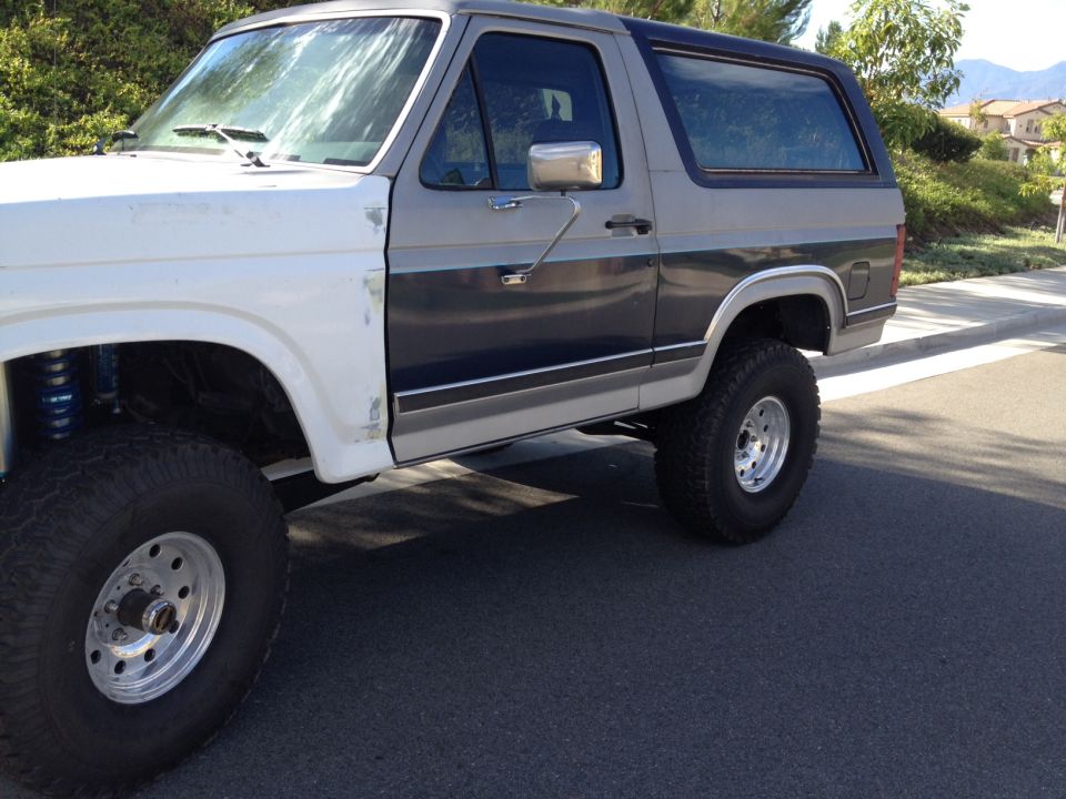 White and grey Ford Bronco with aftermarket wheels and suspension, viewed from the front quarter