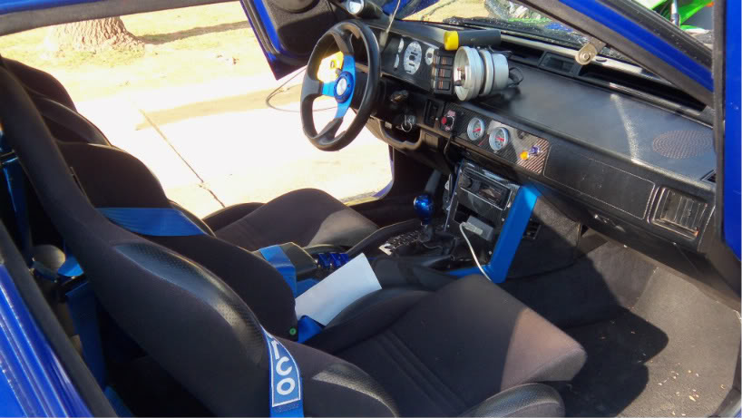 Blue car interior with racing seats, aftermarket steering wheel, and gauges. The dashboard shows a 1989 model year