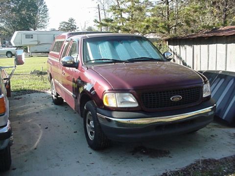 1979 Ford Bronco - This maroon Ford F-150 pickup truck is parked in a driveway with a camper trailer in the background.