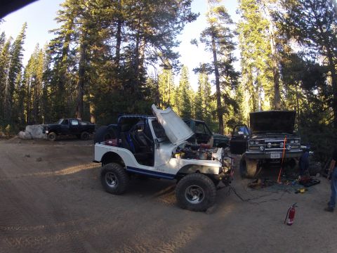 1989 Ford Bronco - A group of off-road vehicles are gathered in a forest clearing, with mechanics attending to engines and repairs.