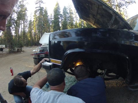 1989 Ford Bronco - People are gathered around a black SUV, working on its undercarriage, with a Jeep nearby.