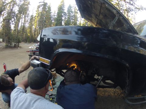 1989 Ford Bronco - Men are welding or grinding on the suspension of a black truck outdoors.
