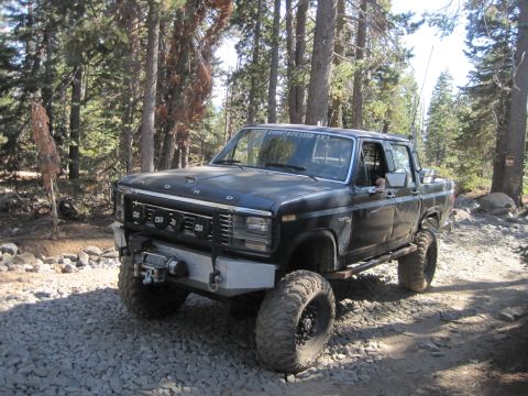 1989 Ford Bronco - Modified black Ford pickup truck parked on a rocky forest road.