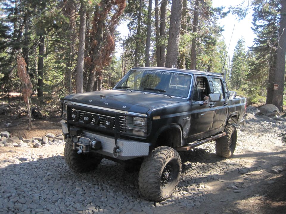 Black Ford pickup truck with off-road tires and winch on a gravel road in a forest