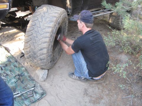1989 Ford Bronco - A person is crouched down, appearing to work on a large tire, possibly changing it in an outdoor setting.