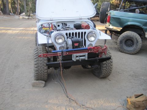 1989 Ford Bronco - A white Jeep with its hood up reveals its engine and a winch mounted on the front bumper, with a green Ford Bronco parked behind it.