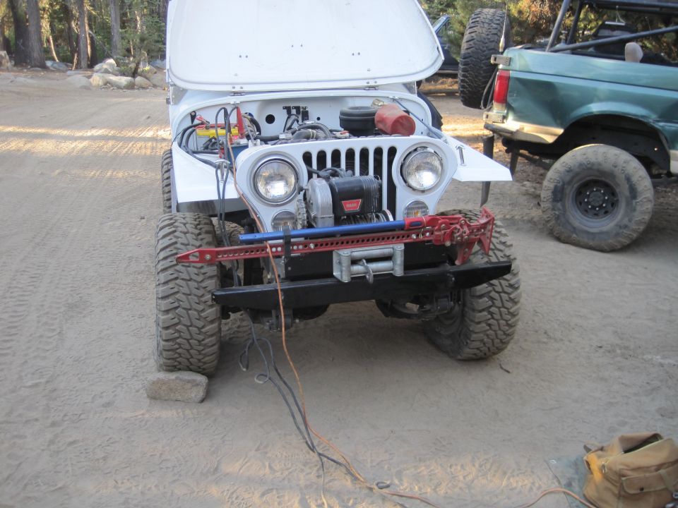 White Jeep with hood open, showing engine and winch. Green Ford Bronco in background