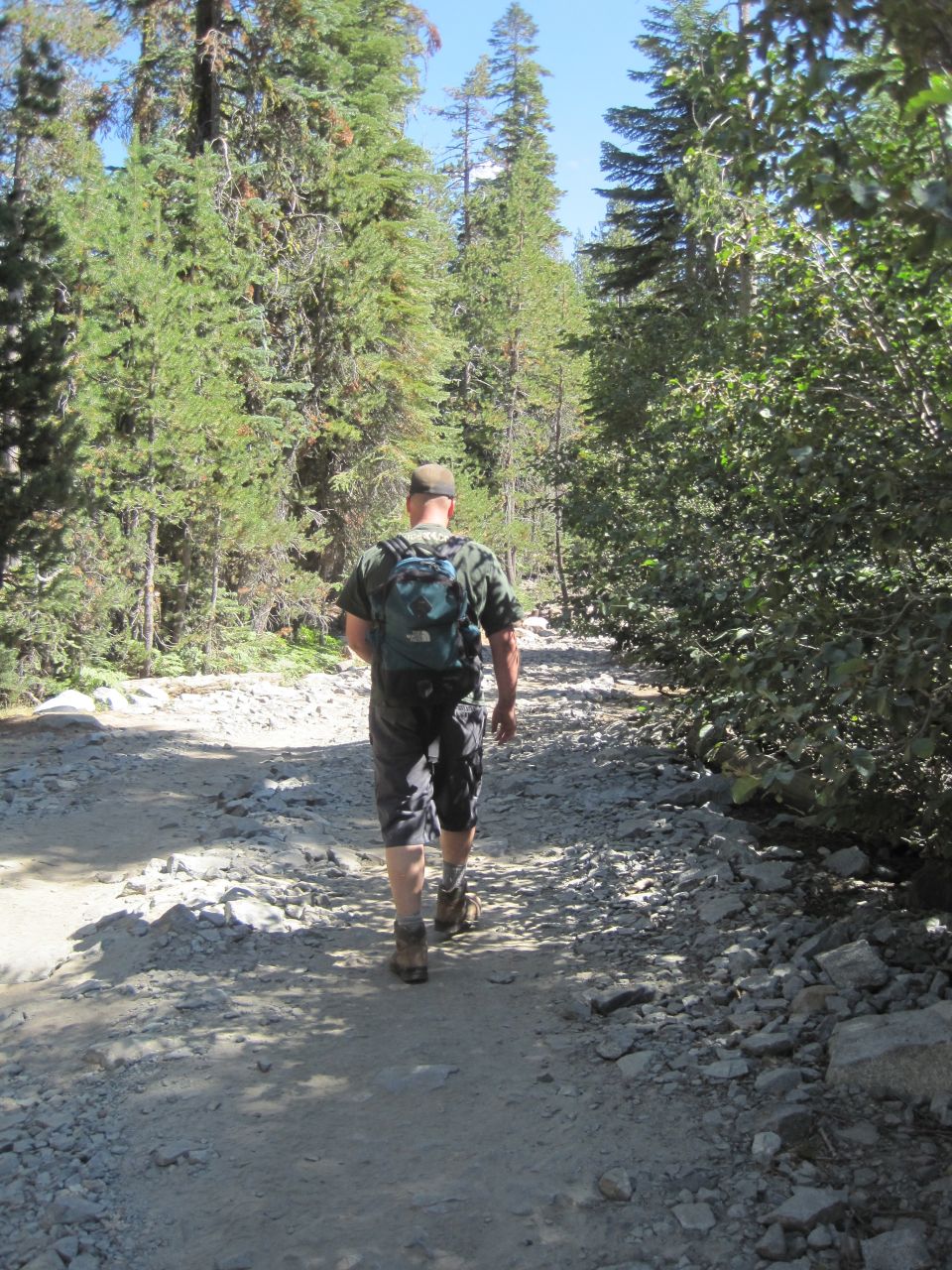 Guy with a backpack walks down a rocky, wooded trail