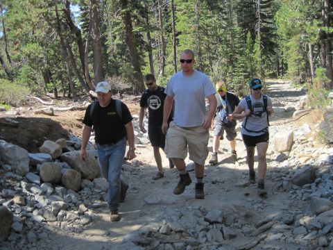 1989 Ford Bronco - A group of hikers navigates a rough, rocky path through a forest on a sunny day.