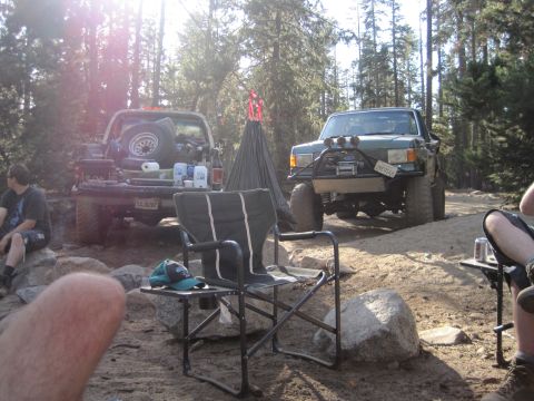 1989 Ford Bronco - Two trucks are parked at a campsite in a forest, with a tent and camping chairs set up.