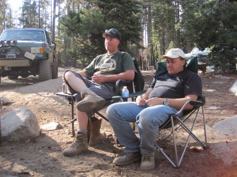 1989 Ford Bronco - Two men are relaxing in camping chairs at a campsite, with a modified truck visible in the background.
