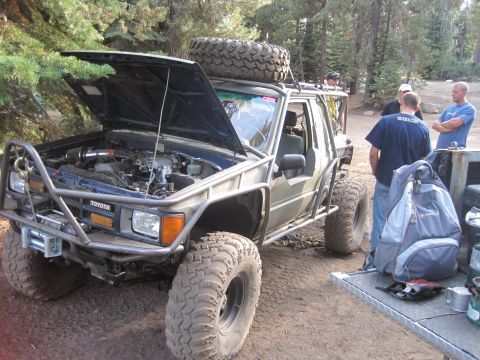 1989 Ford Bronco - Modified Toyota SUV with extensive off-road modifications, including a roll cage and winch, parked outdoors with the hood open.