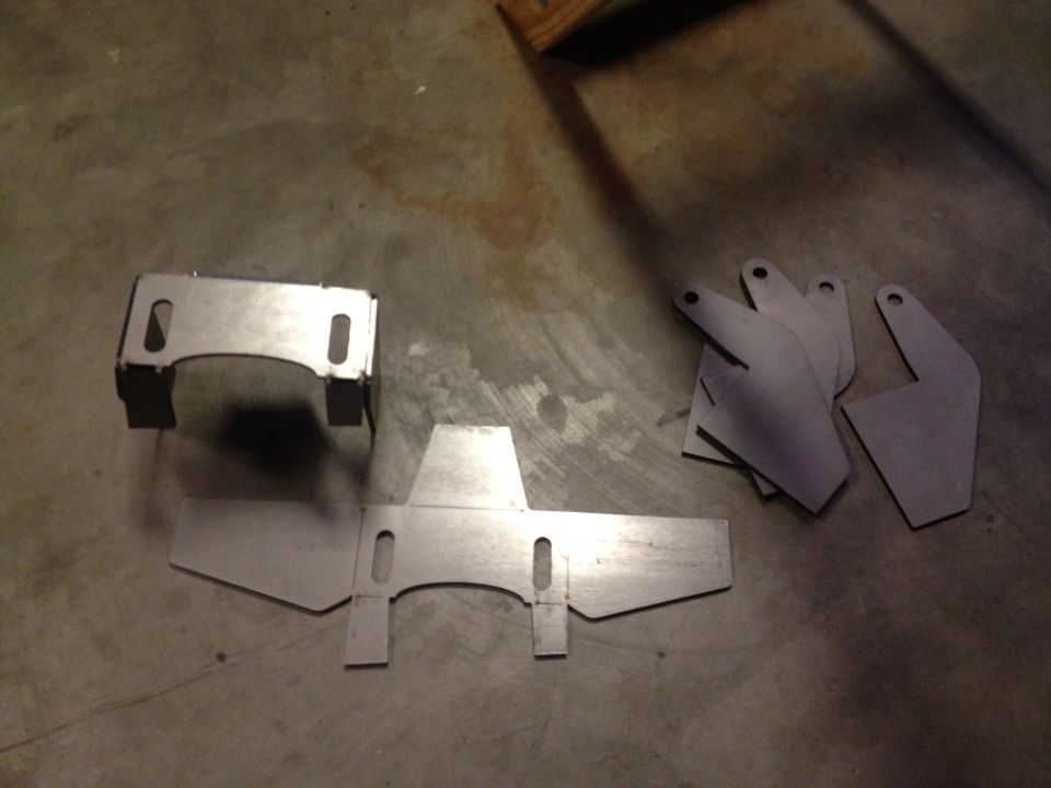 Metal brackets and flat pieces laid out on a concrete floor