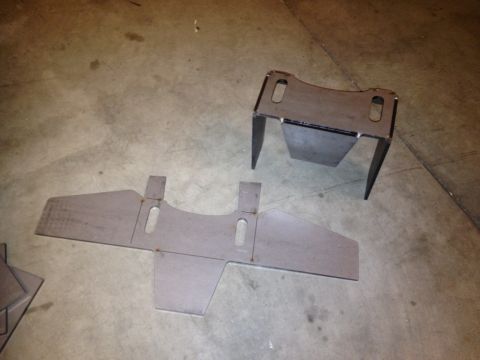 1965 Ford Mustang - Two unpainted metal automotive parts are laid out on a concrete floor, likely for installation or fabrication.
