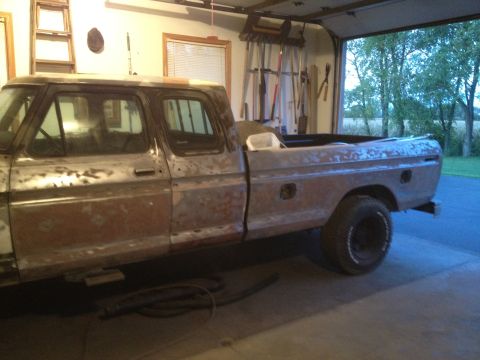 1979 Ford F-350 - A four-door pickup truck, stripped down to its metal body, sits in a garage with the door open.