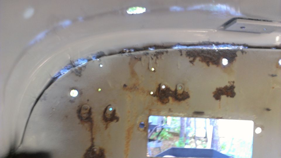 close-up of a rusty, white metal panel with several holes and some blue welding marks