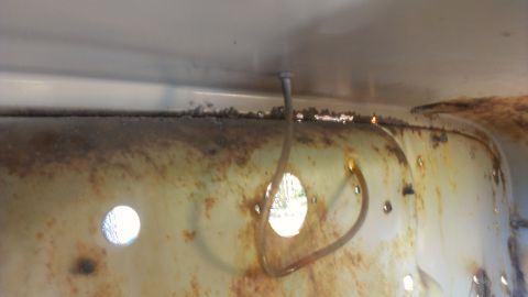 1978 Ford Bronco - Close-up of a heavily rusted interior panel with visible hoses and holes.